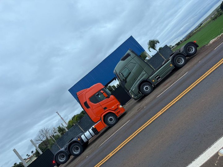 Cavalos mecânicos Scania laranja e Volvo verde estacionados à beira da rodovia